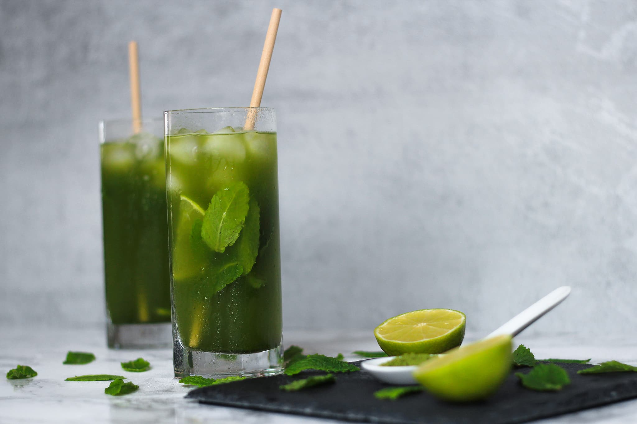 Zwei Gläser Matcha Ice Tea mit frischen Minzblättern und einer Zitrone